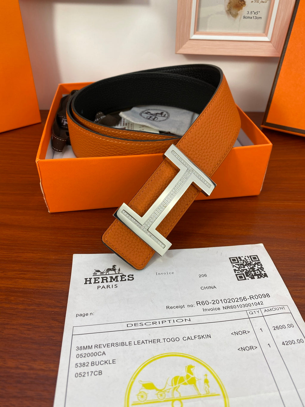 Reversible leather belt, orange strap with silver-tone H buckle, in open box.
