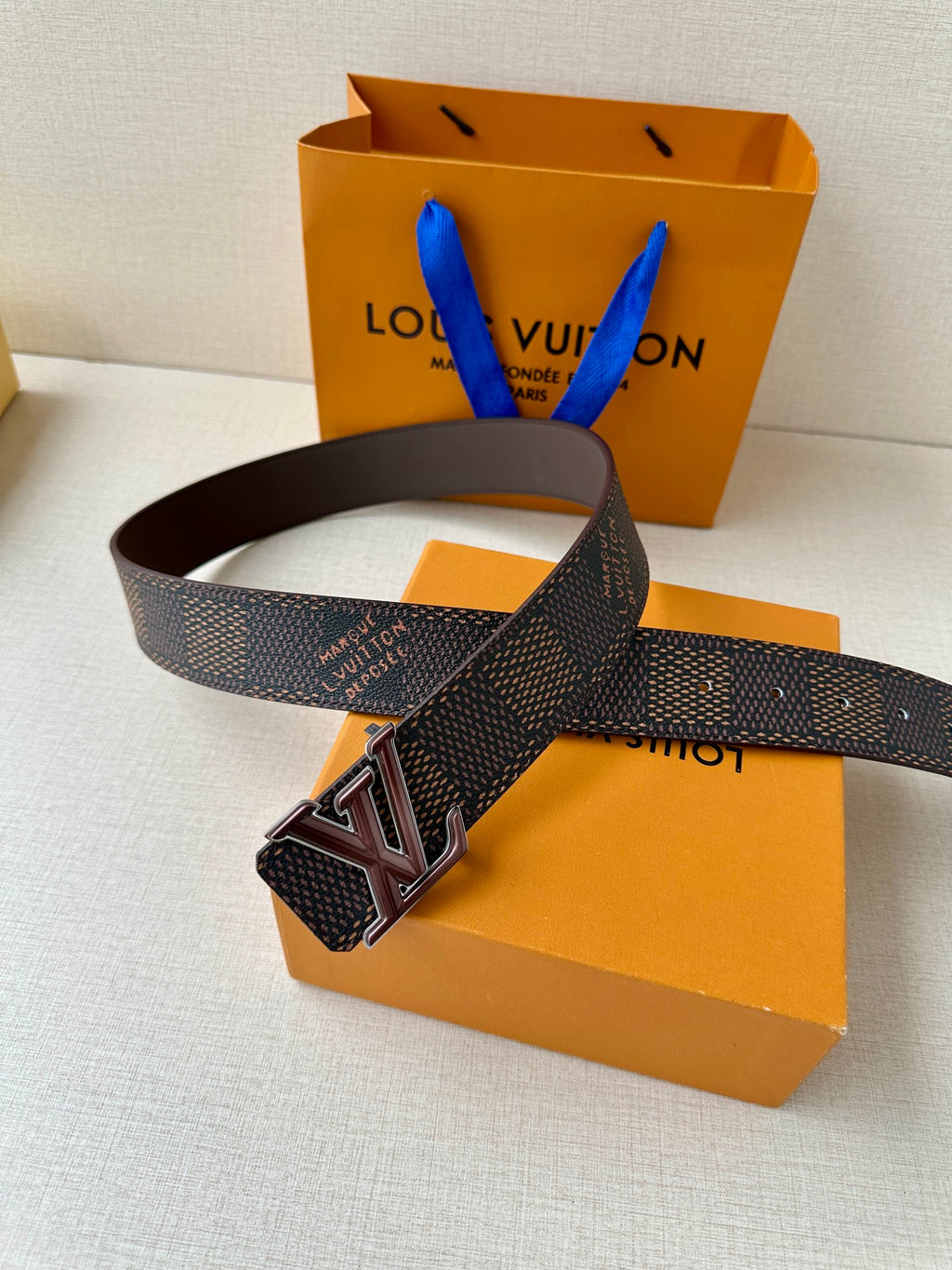 LV belt with dark monogram strap and brown leather buckle, laid across