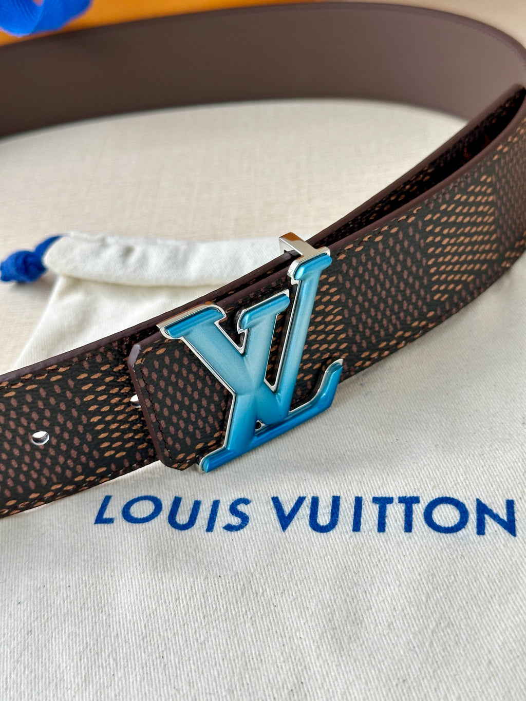 Louis Vuitton belt detail: dark monogram strap with blue LV buckle