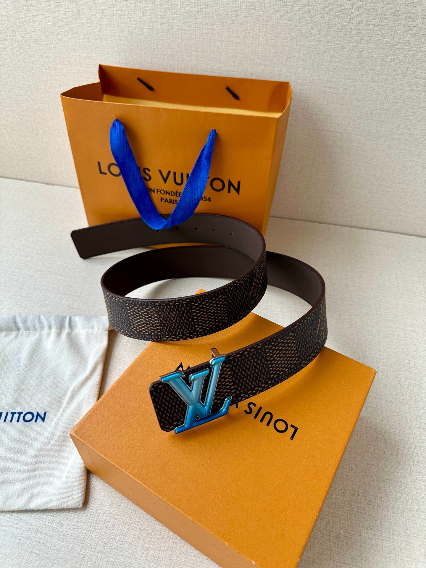 Louis Vuitton belt laid on orange box and white cloth, dark monogram blue LV buckle