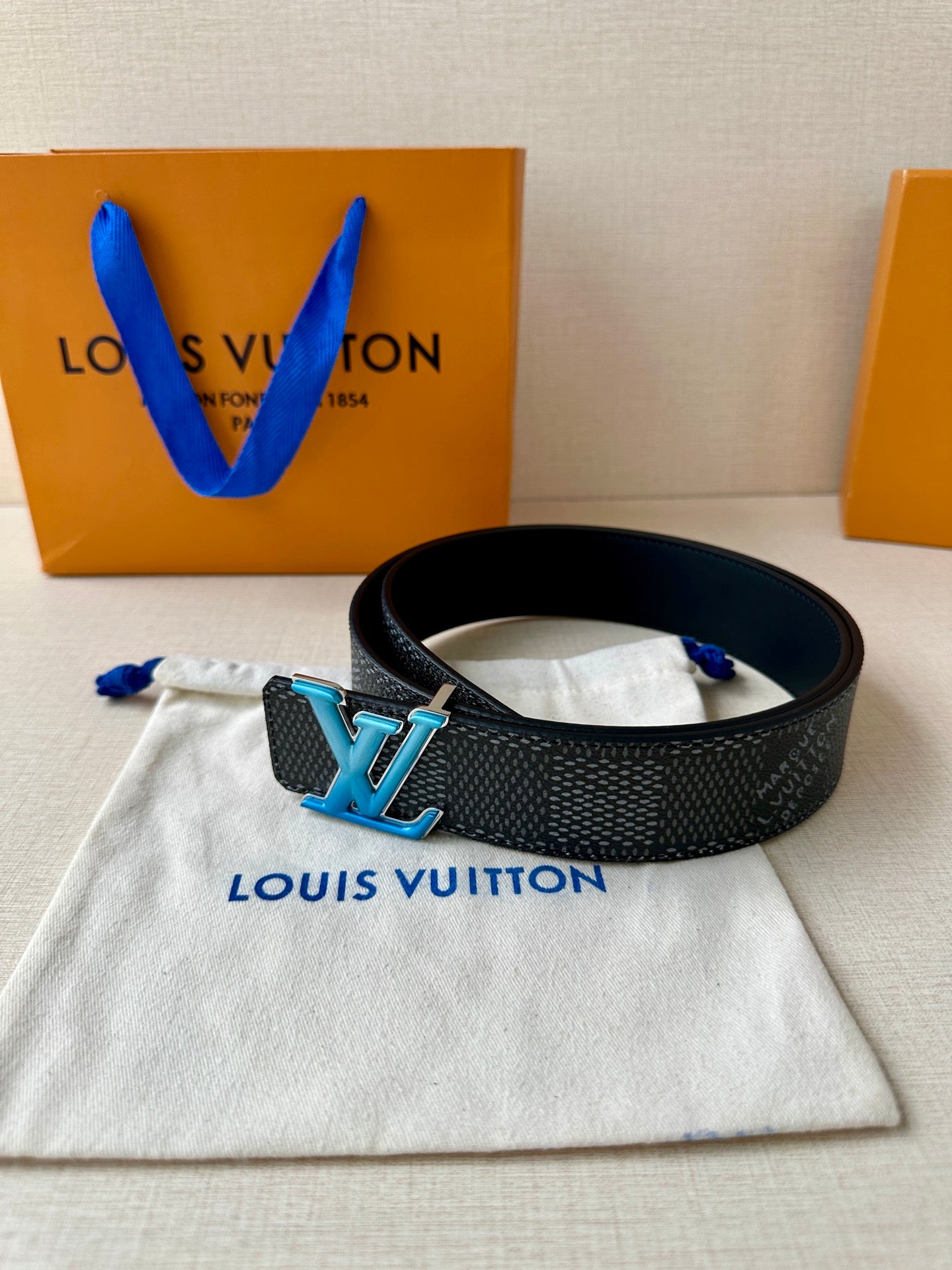 Louis Vuitton belt on white pouch with dark strap and blue LV buckle clasp.