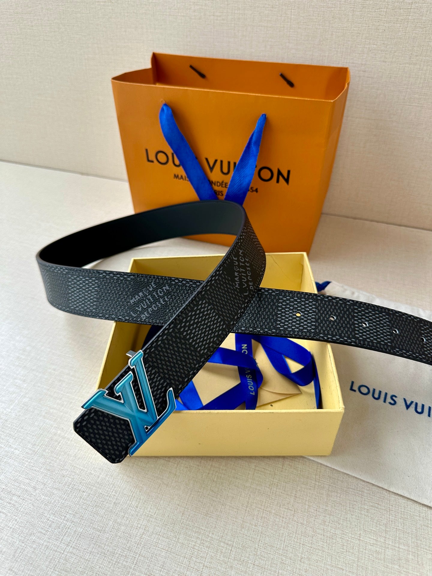 Louis Vuitton belt dark leather strap with blue LV buckle, laid across box contents.
