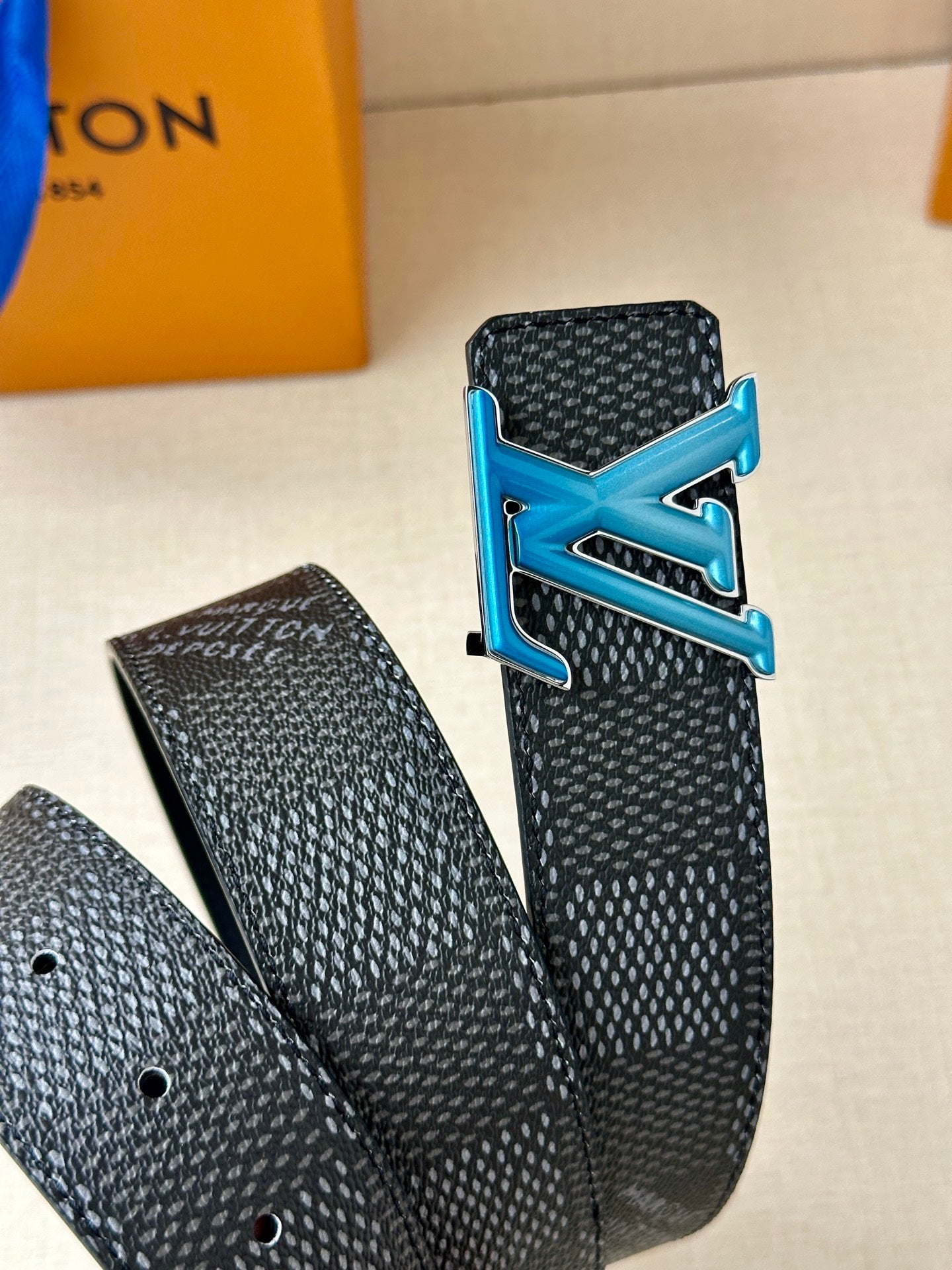 Louis Vuitton belt close-up of dark strap with blue LV buckle and punched adjustment holes.