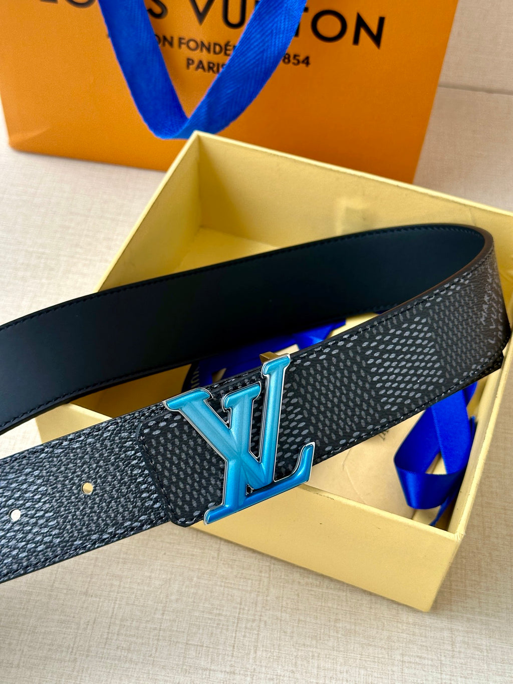 Louis Vuitton belt with dark patterned strap and blue LV buckle, shown at an angle.