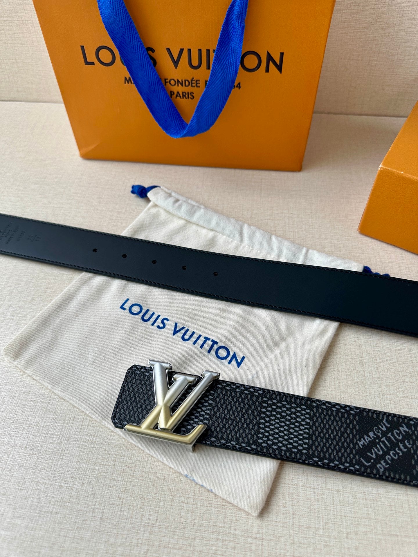 Dark textured belt laid flat with silver LV buckle and punched holes