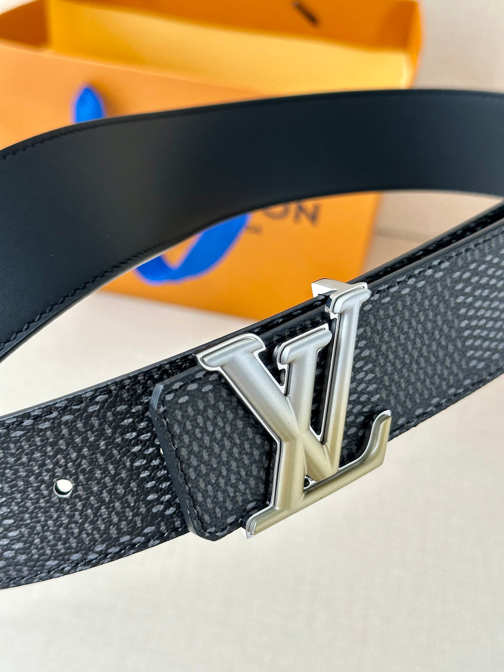 Dark textured belt with silver LV buckle close-up and embossed pattern