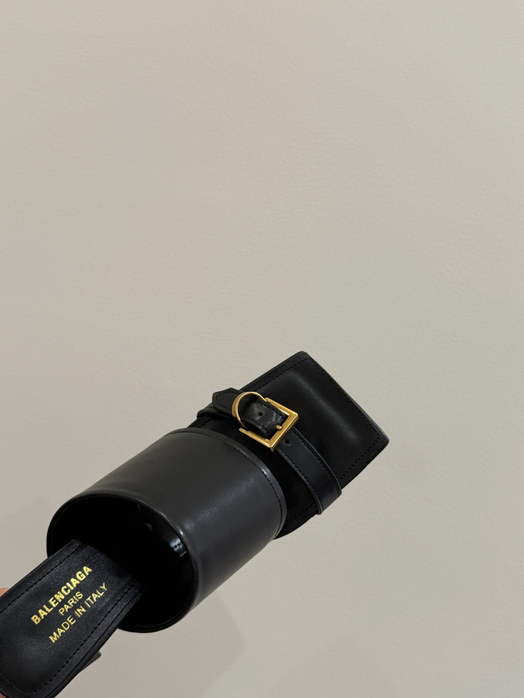 Black leather slide sandal with square gold buckle, close-up of strap