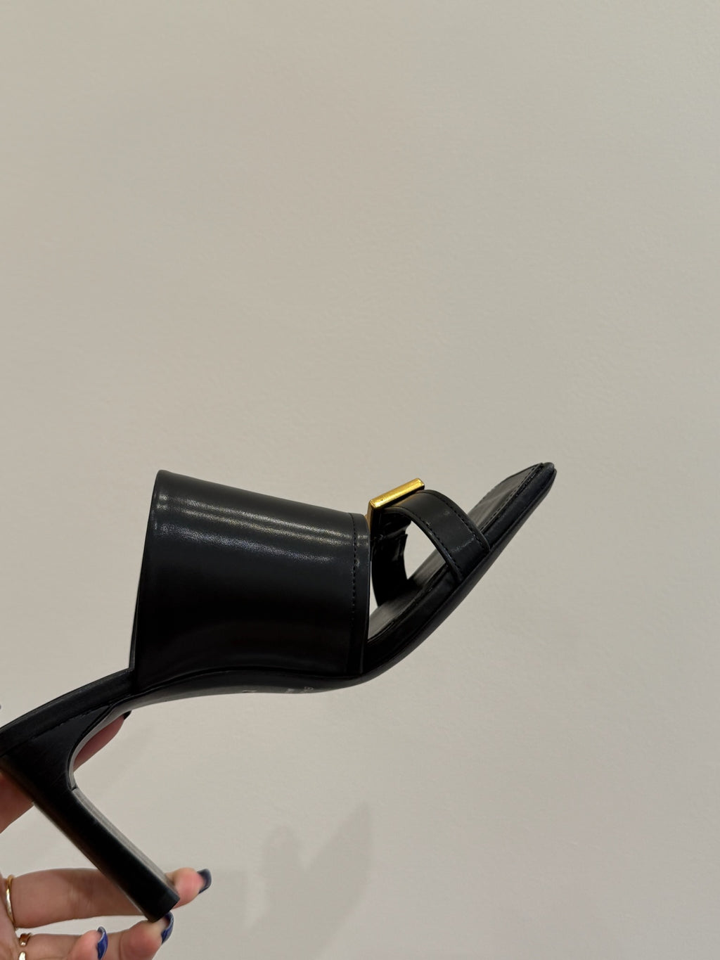 Black leather mule sandal with gold buckle strap, side view of heel
