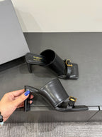 Black leather mule sandals with gold buckle, one held in hand