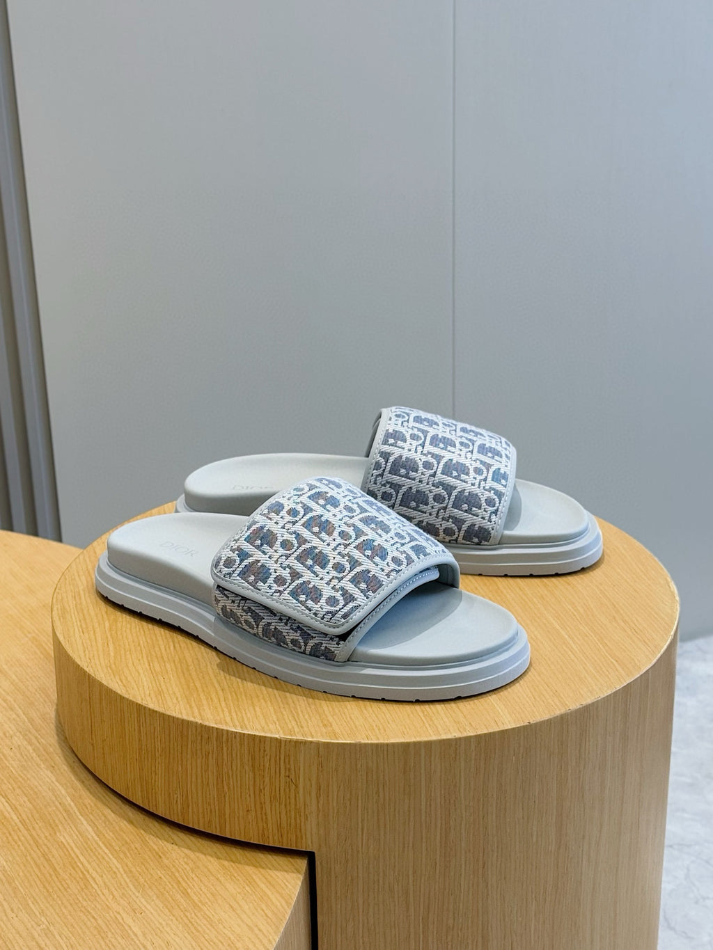 Dior slide sandals, navy Oblique-print straps with light blue soles, angled pair on stand