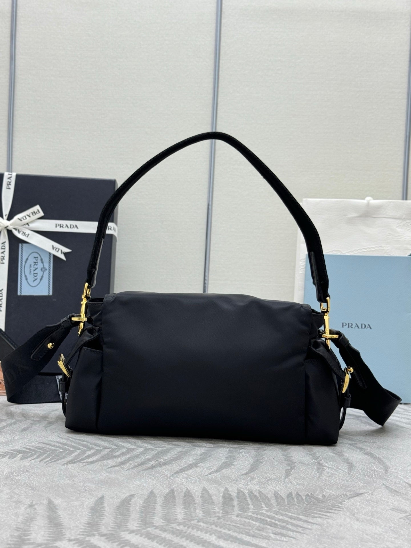 Prada black nylon shoulder bag with curved top handle, crossbody strap, and gold accents