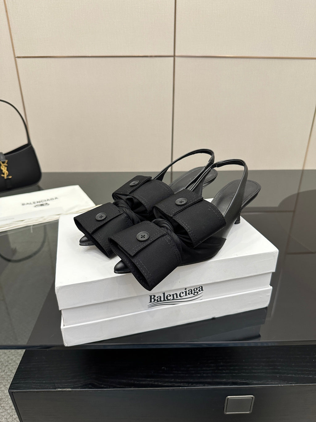 Black mules with bow-like wrap straps and low block heel, on white box