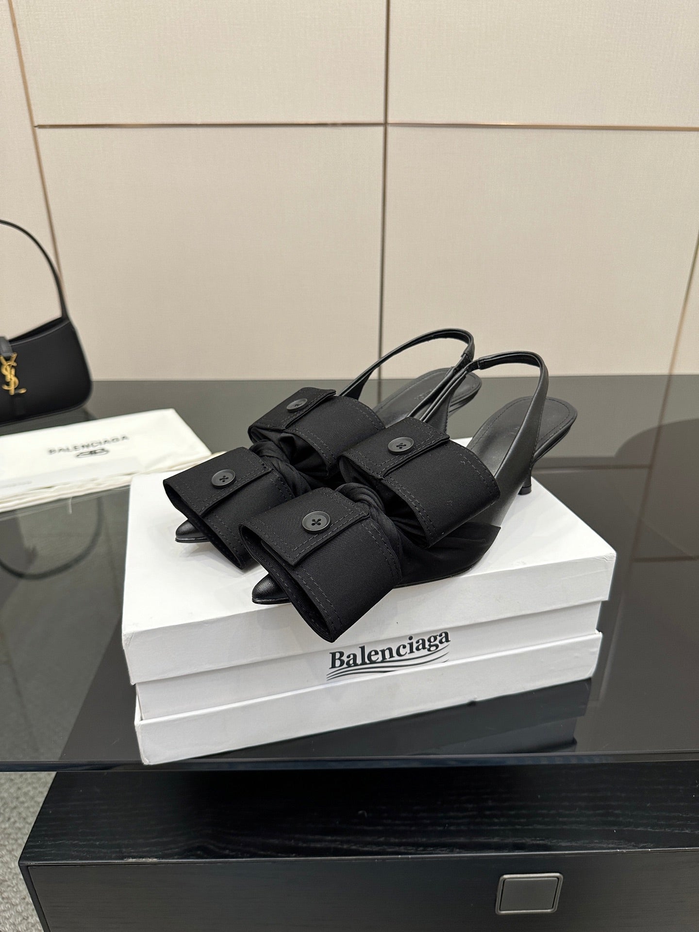 Black mules with bow-like wrap straps and low block heel, on white box