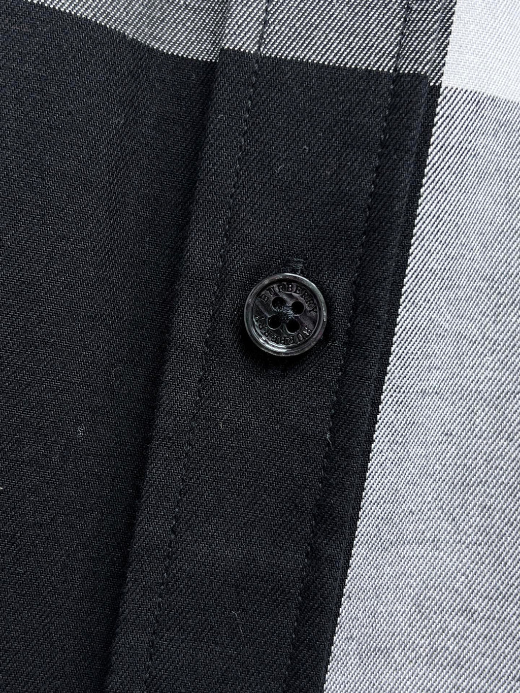 Round black button on front placket of a black-and-white plaid button-up shirt