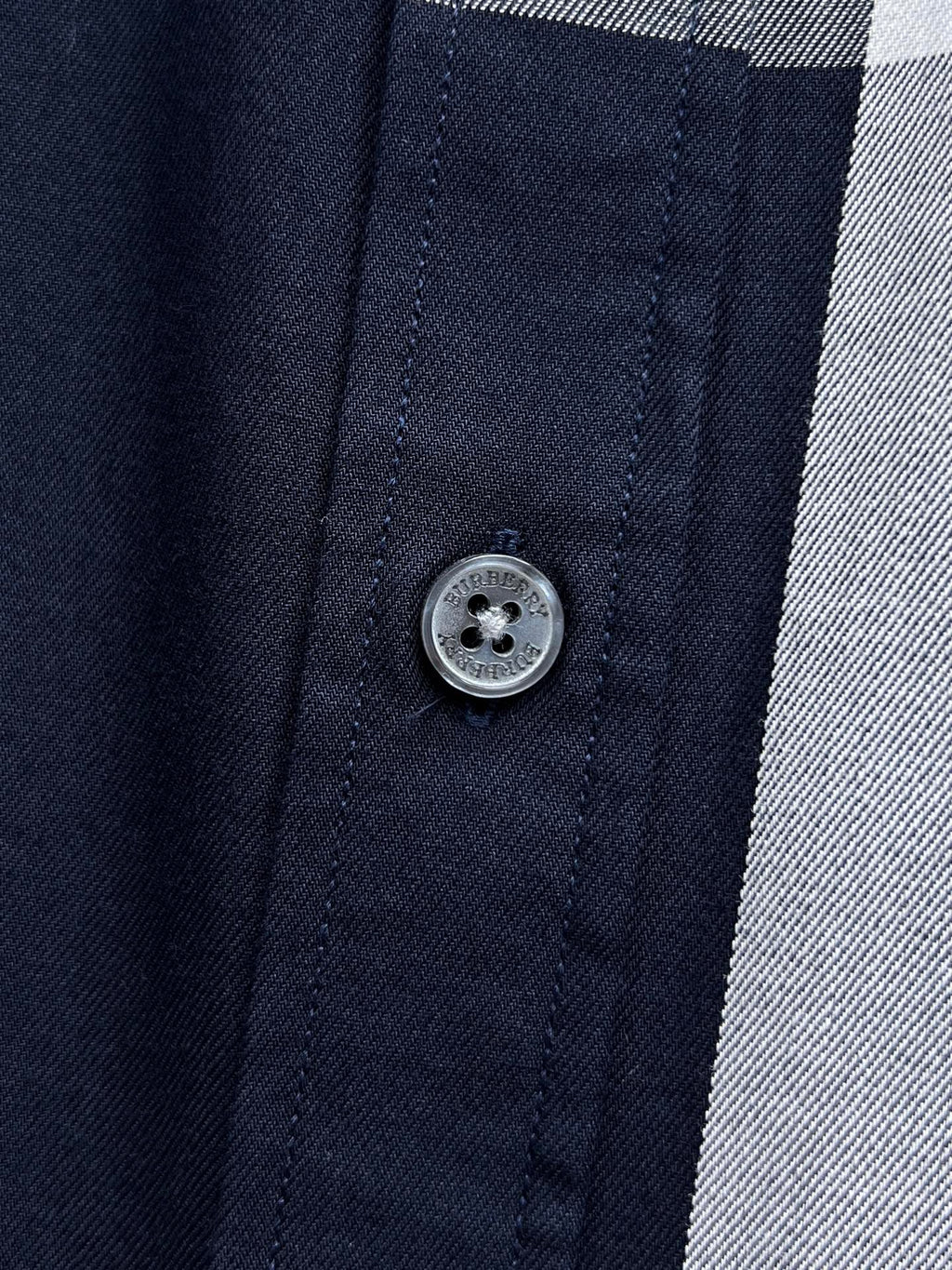 Burberry shirt button close-up on navy fabric with stitched placket