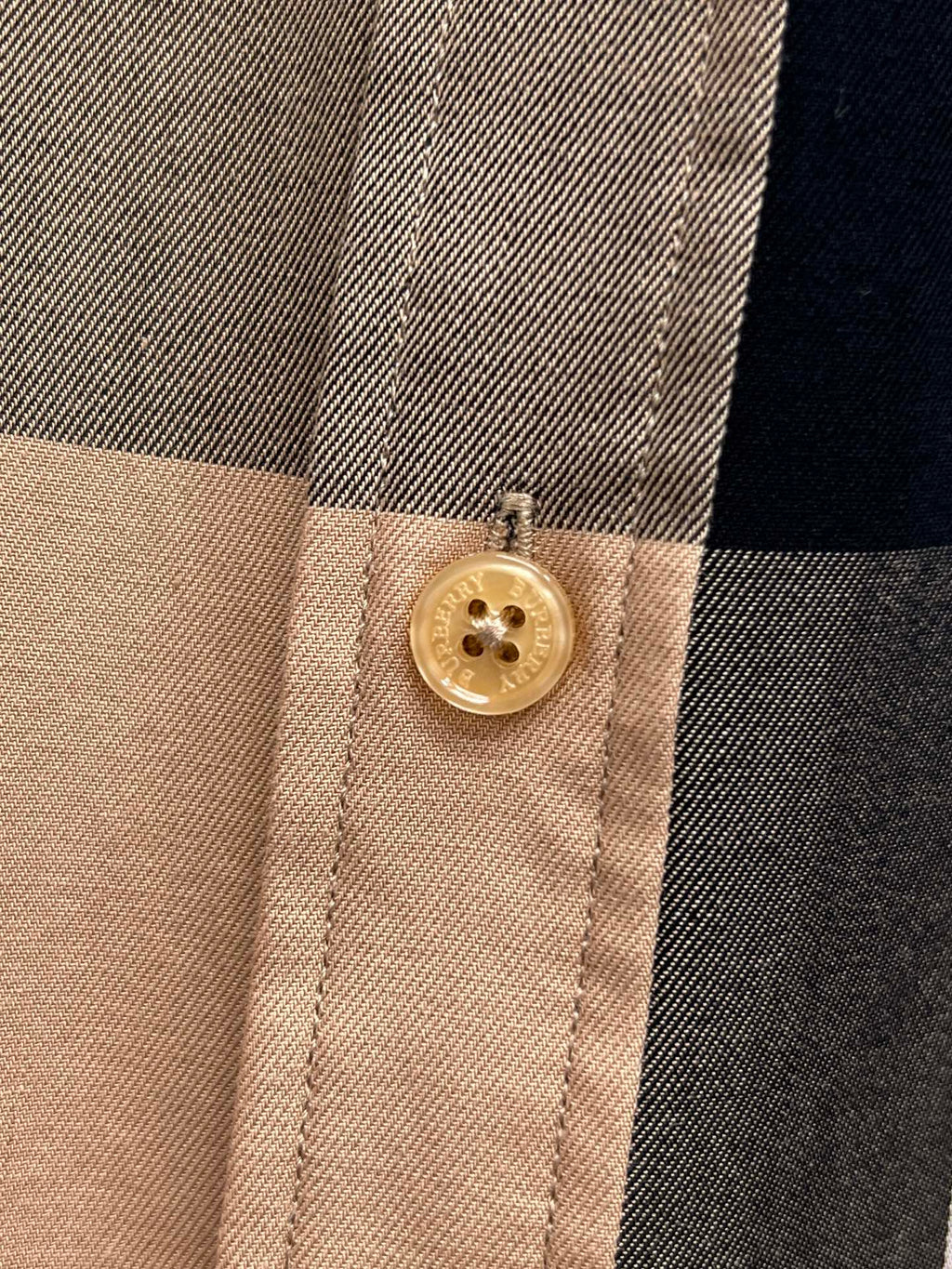 Burberry plaid shirt cuff with gold button on beige fabric