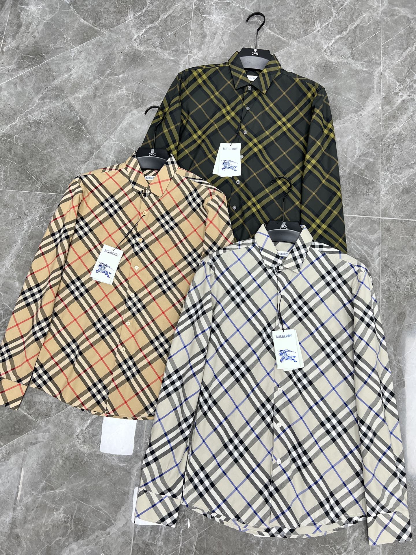 Three plaid long-sleeve button-up shirts on hangers with product tags