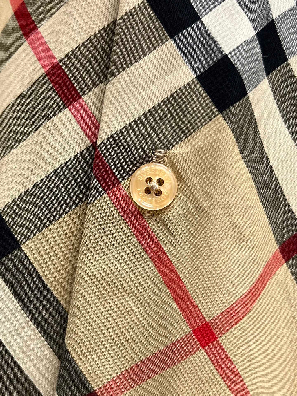 Burberry plaid shirt with round gold button on beige, black, and red pattern