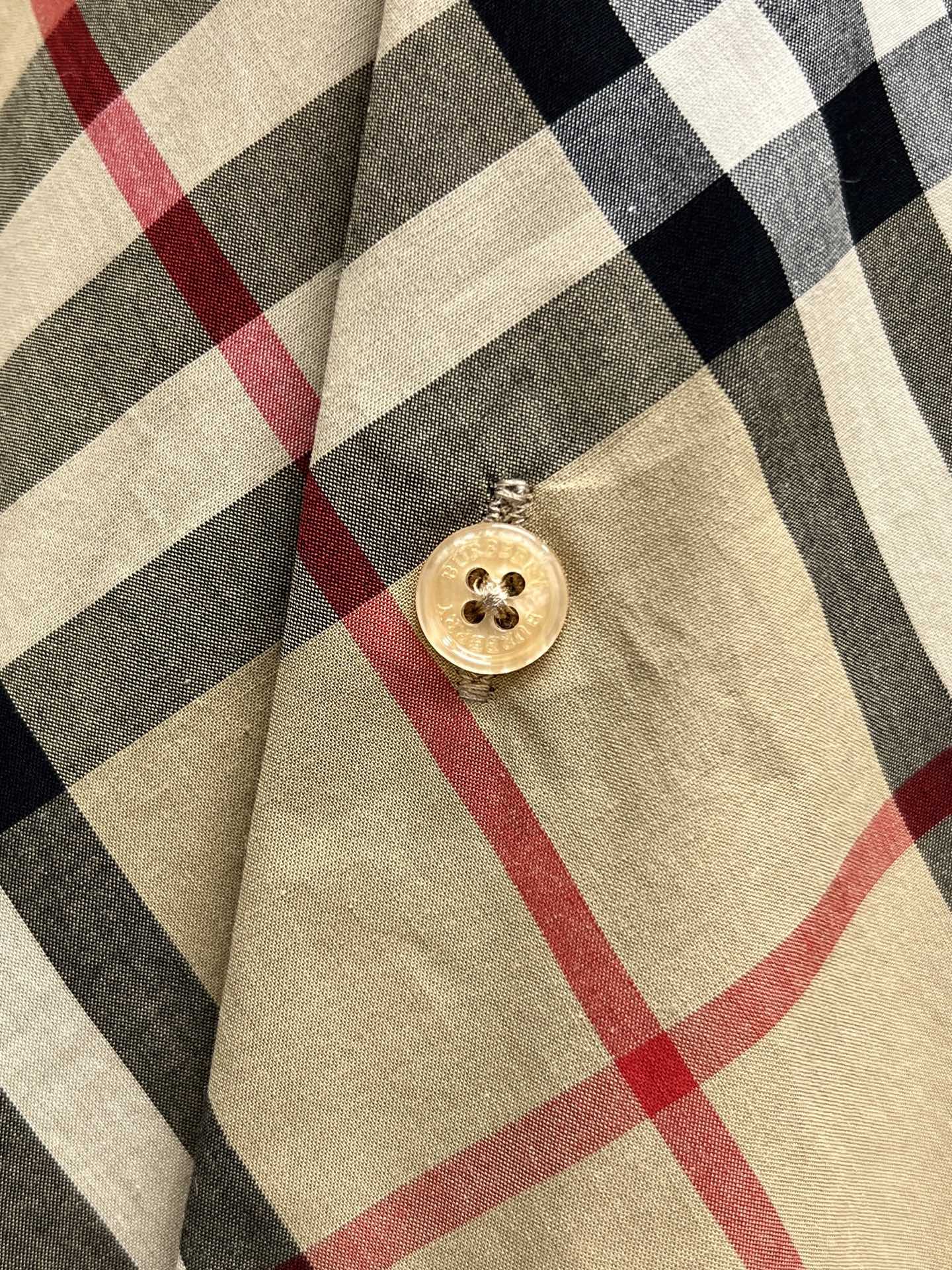 Burberry plaid shirt with round gold button on beige, black, and red pattern