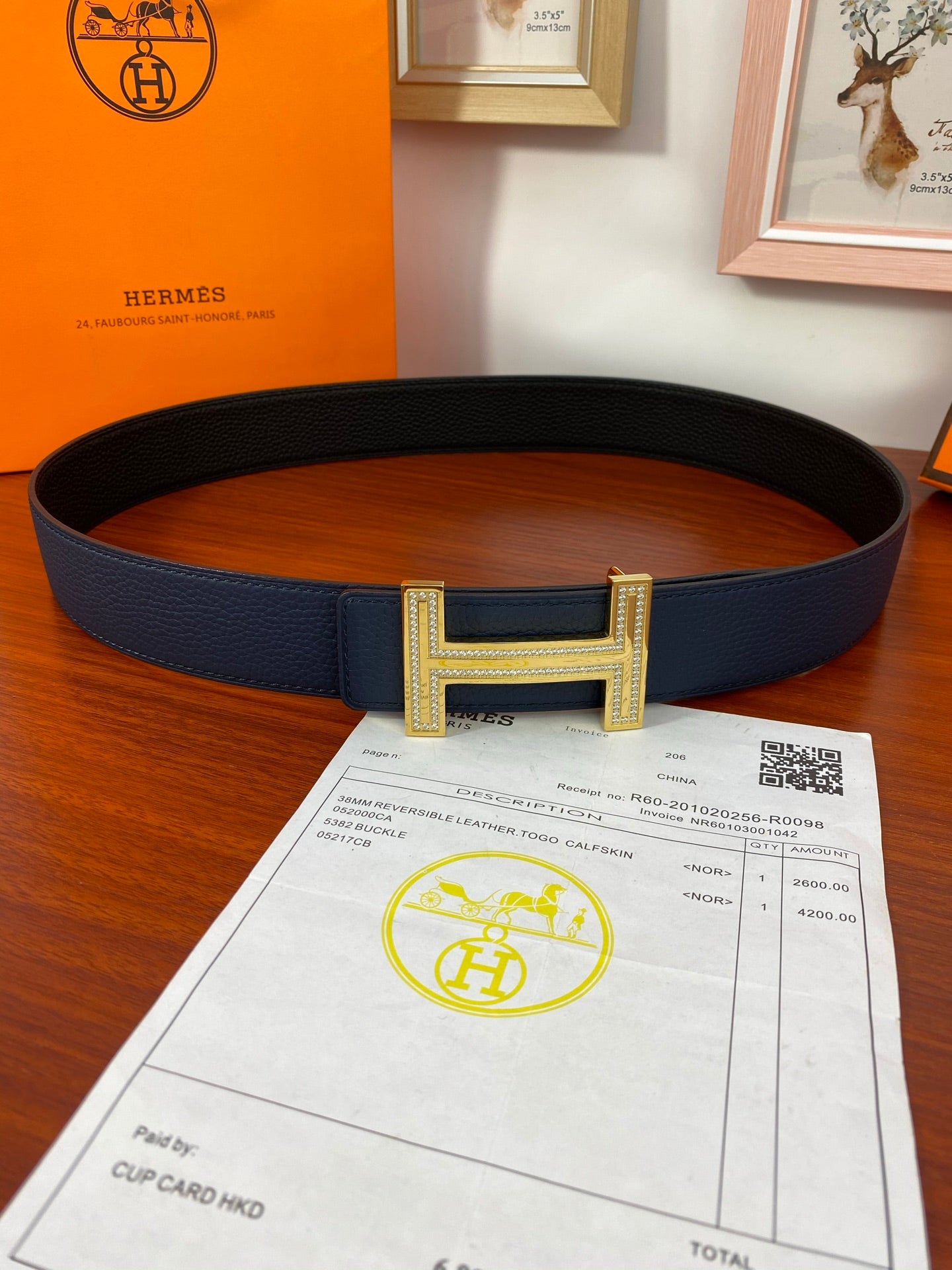 Blue leather belt with large gold H buckle and centered keeper on strap.