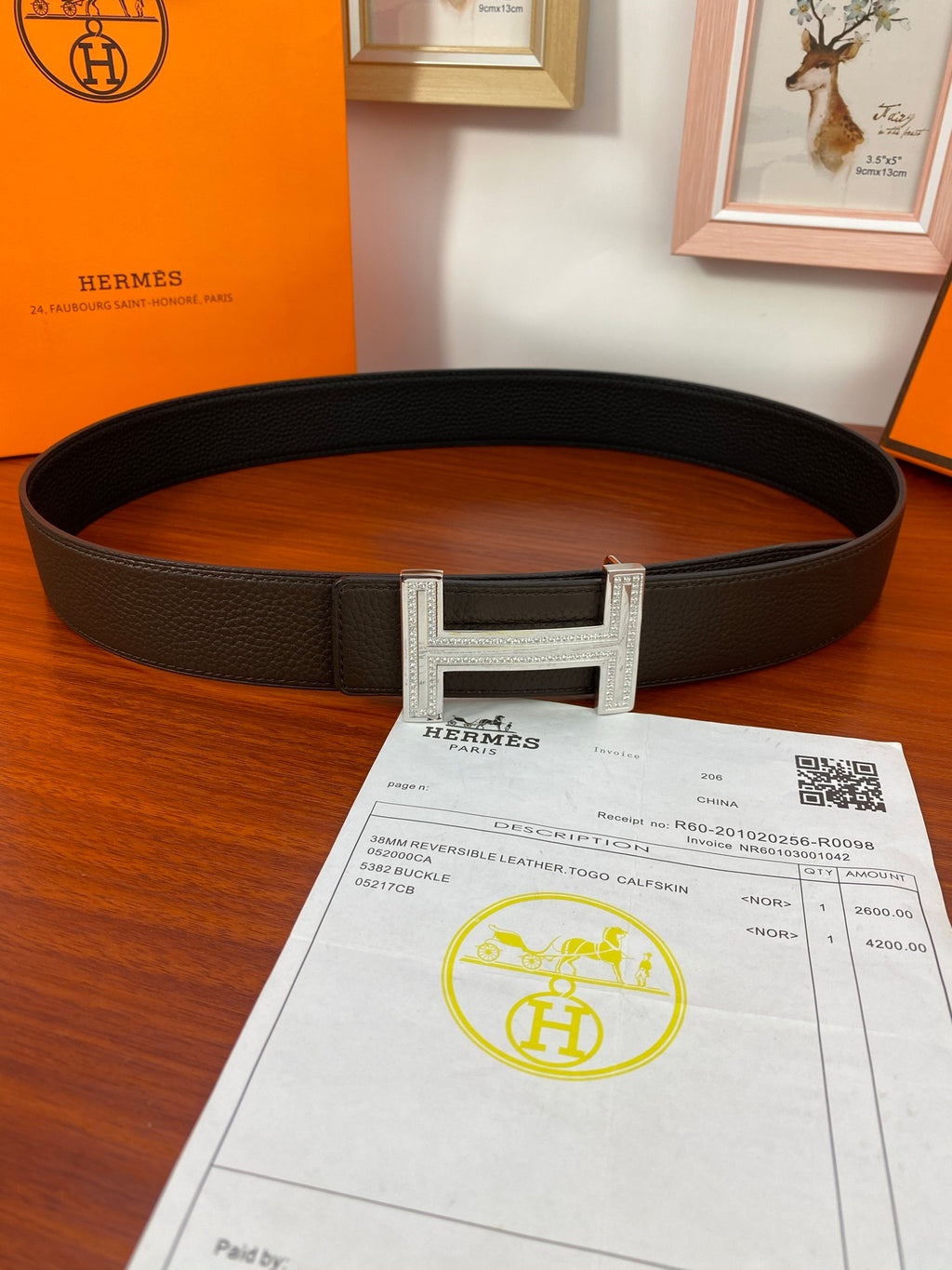 Dark leather belt with silver H buckle and textured strap over receipt