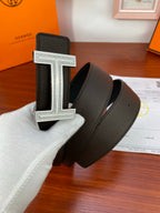Dark leather belt with wide textured strap and silver H buckle in hand
