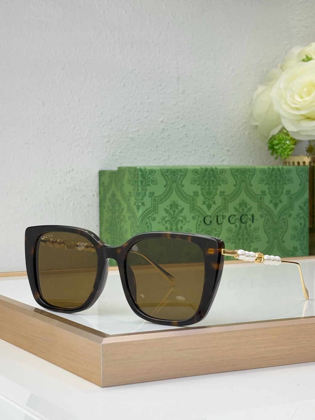 Gucci glasses with brown-tinted lenses, black square frames, and pearl-bead temple detail