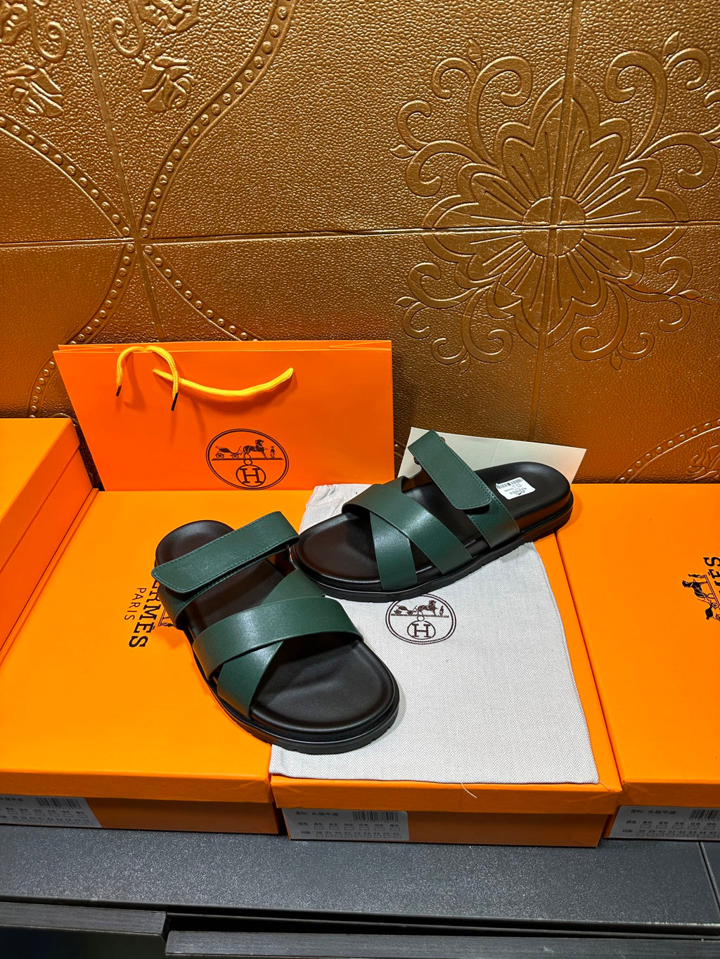 Hermes teal green sandals with wide straps and black sole, shown on packaging