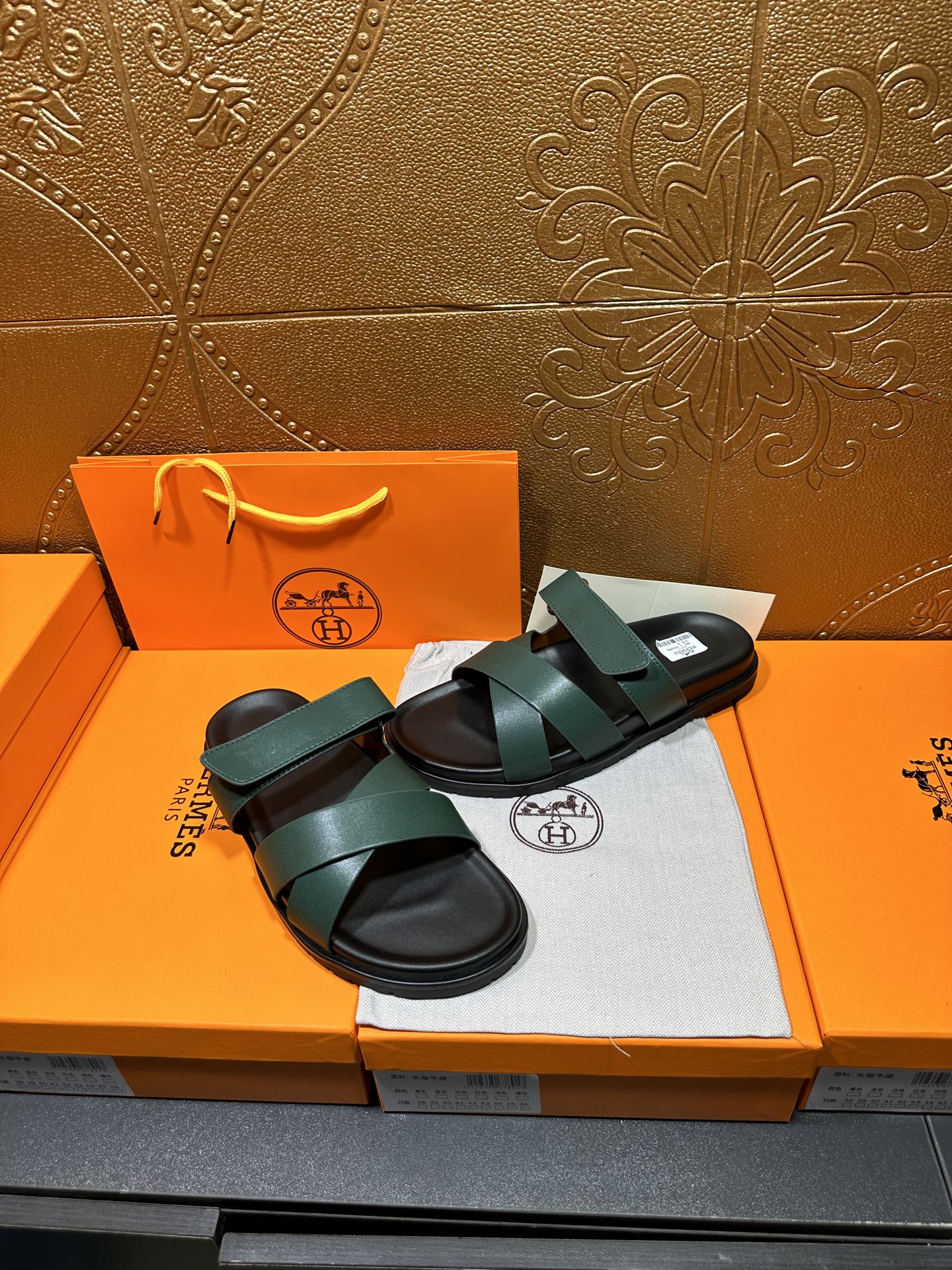 Hermes teal green sandals with wide straps and black sole, shown on packaging