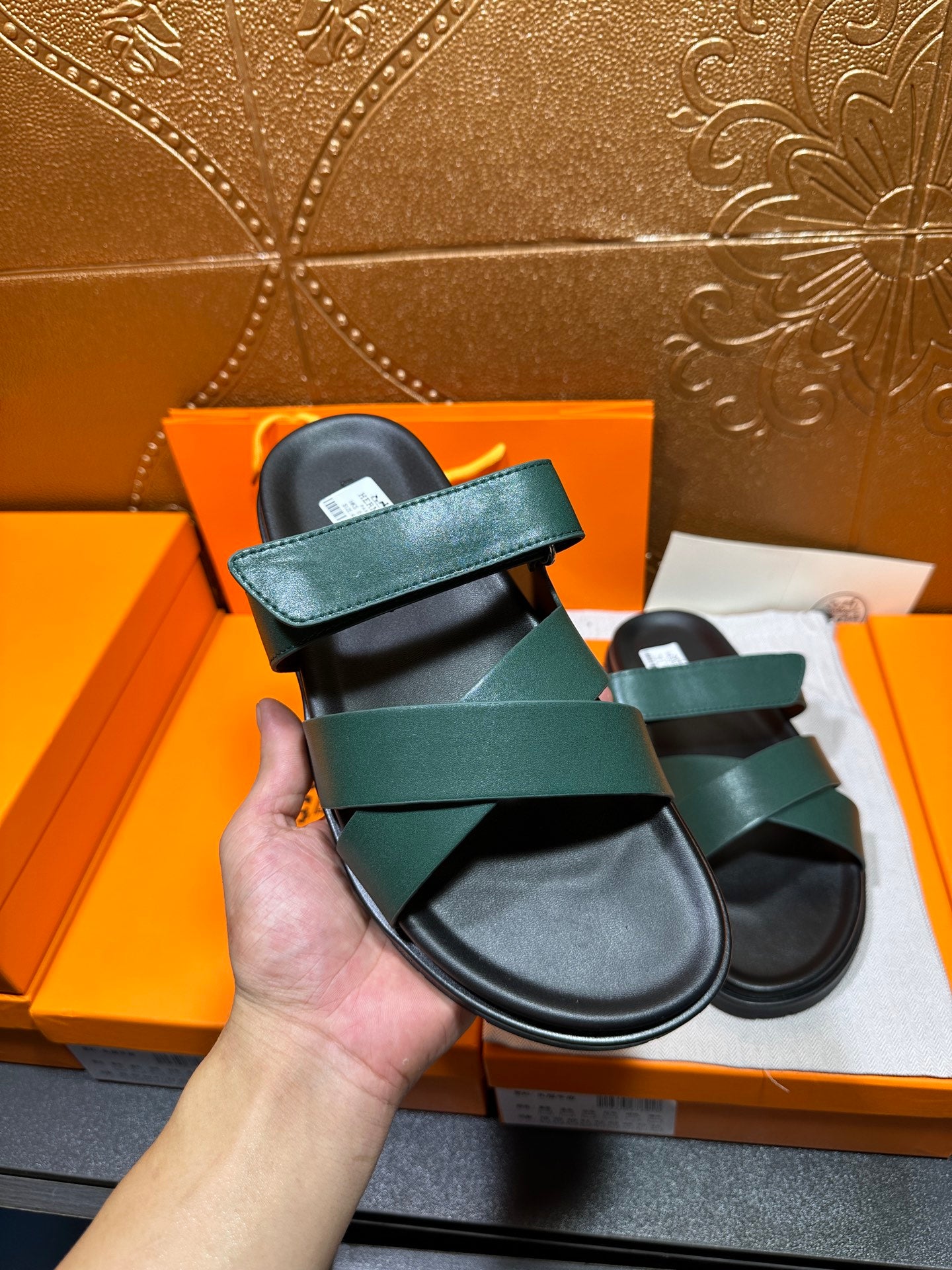 Hermes green slide sandals held in hand, with wide straps and black footbed
