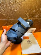 Hermes single slide sandal held in hand, navy straps over black footbed