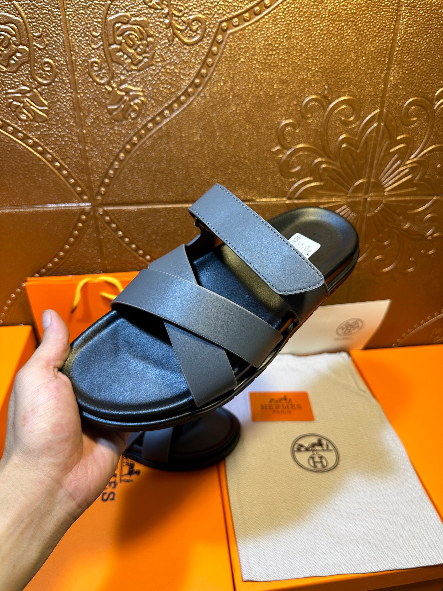 Hermes single slide sandal held in hand, navy straps over black footbed