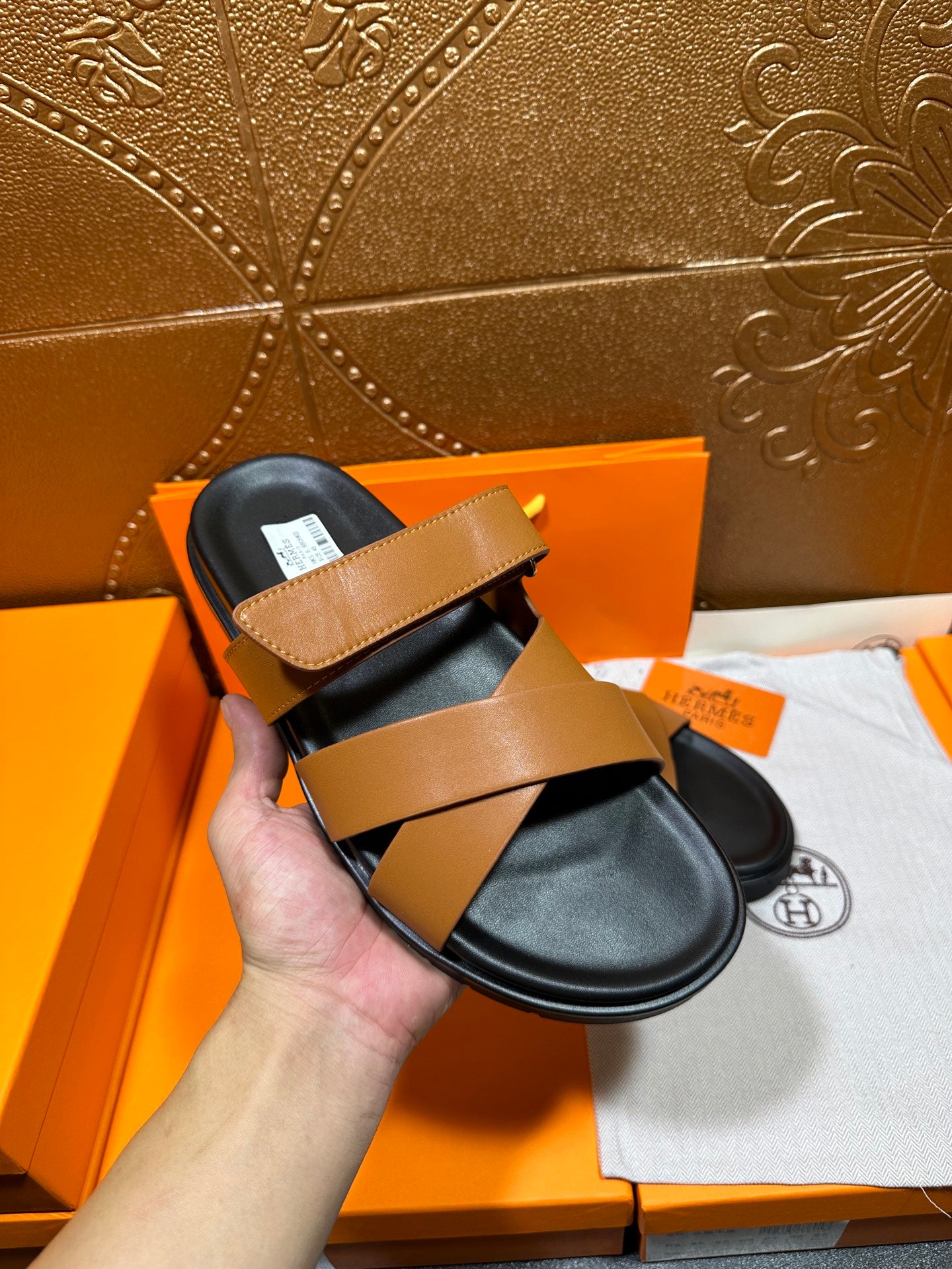 Hermes slide sandals with tan strap and black footbed, held in hand