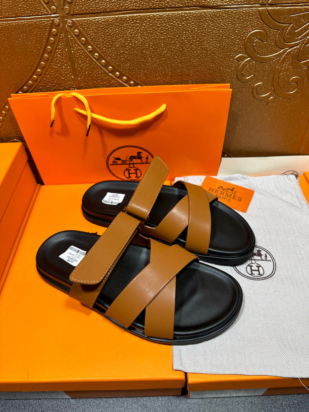 Hermes slide sandals with tan straps and black footbed, angled view