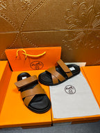 Hermes sandals pair with tan straps and black footbeds, laid on dust bag