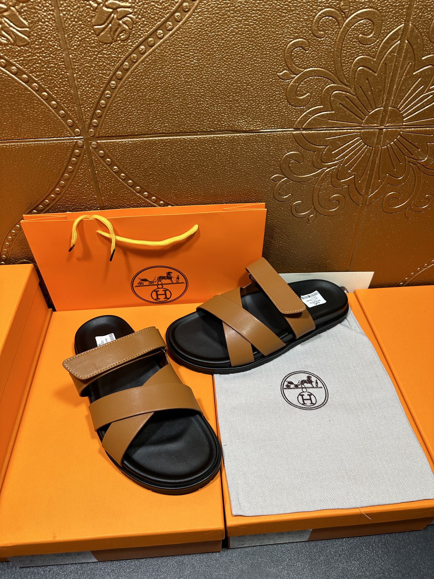 Hermes sandals pair with tan straps and black footbeds, laid on dust bag