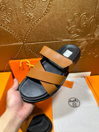 Hermes slide sandals with tan strap and black footbed, angled on box