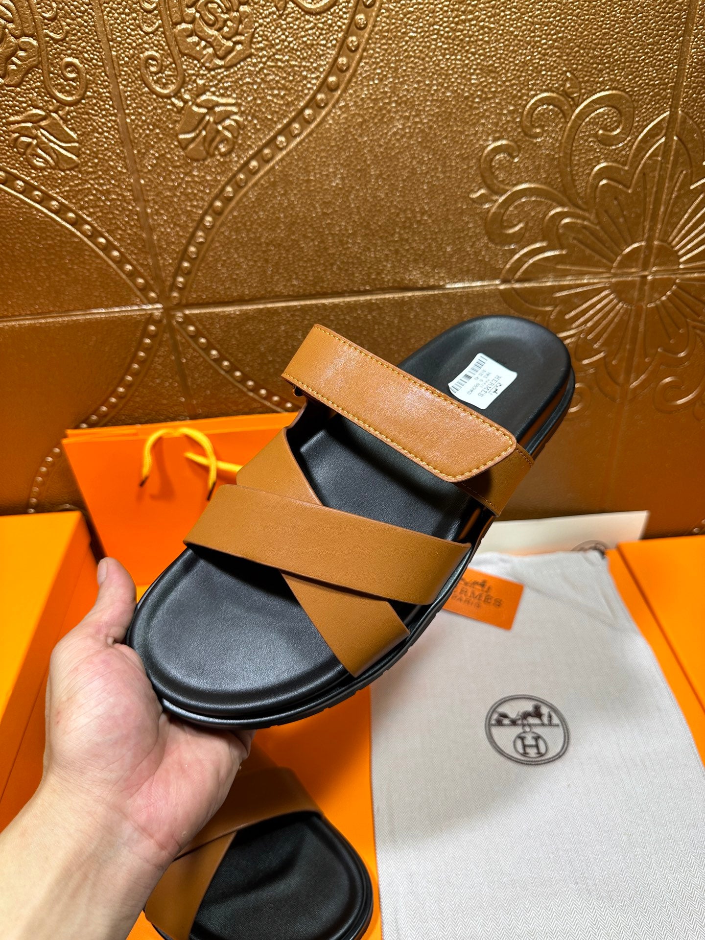 Hermes slide sandals with tan strap and black footbed, angled on box