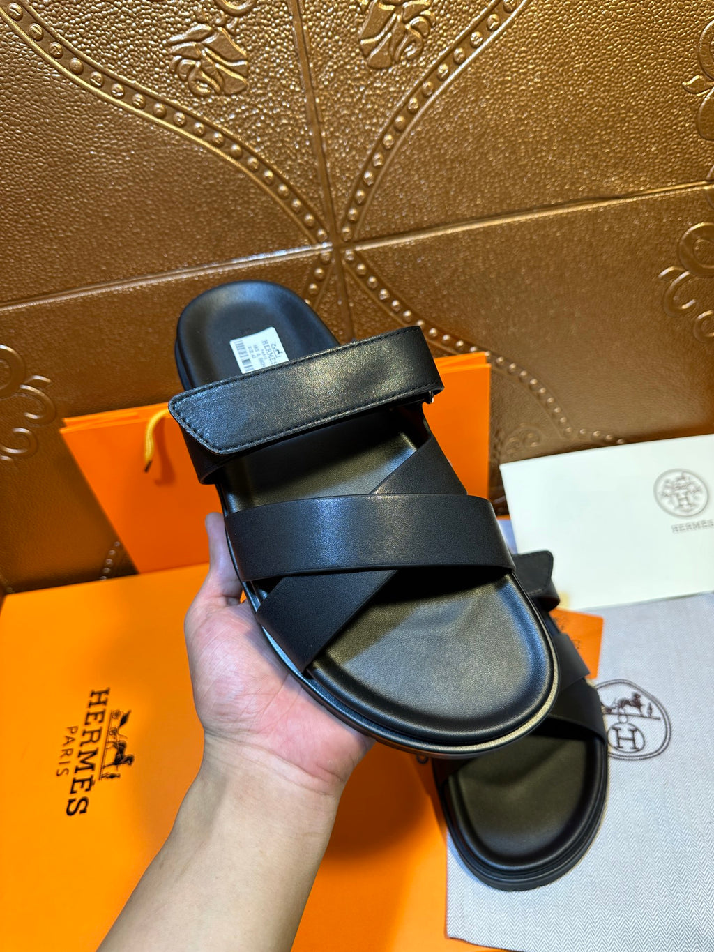 Black leather sandal held up, showing wide strap and cushioned footbed