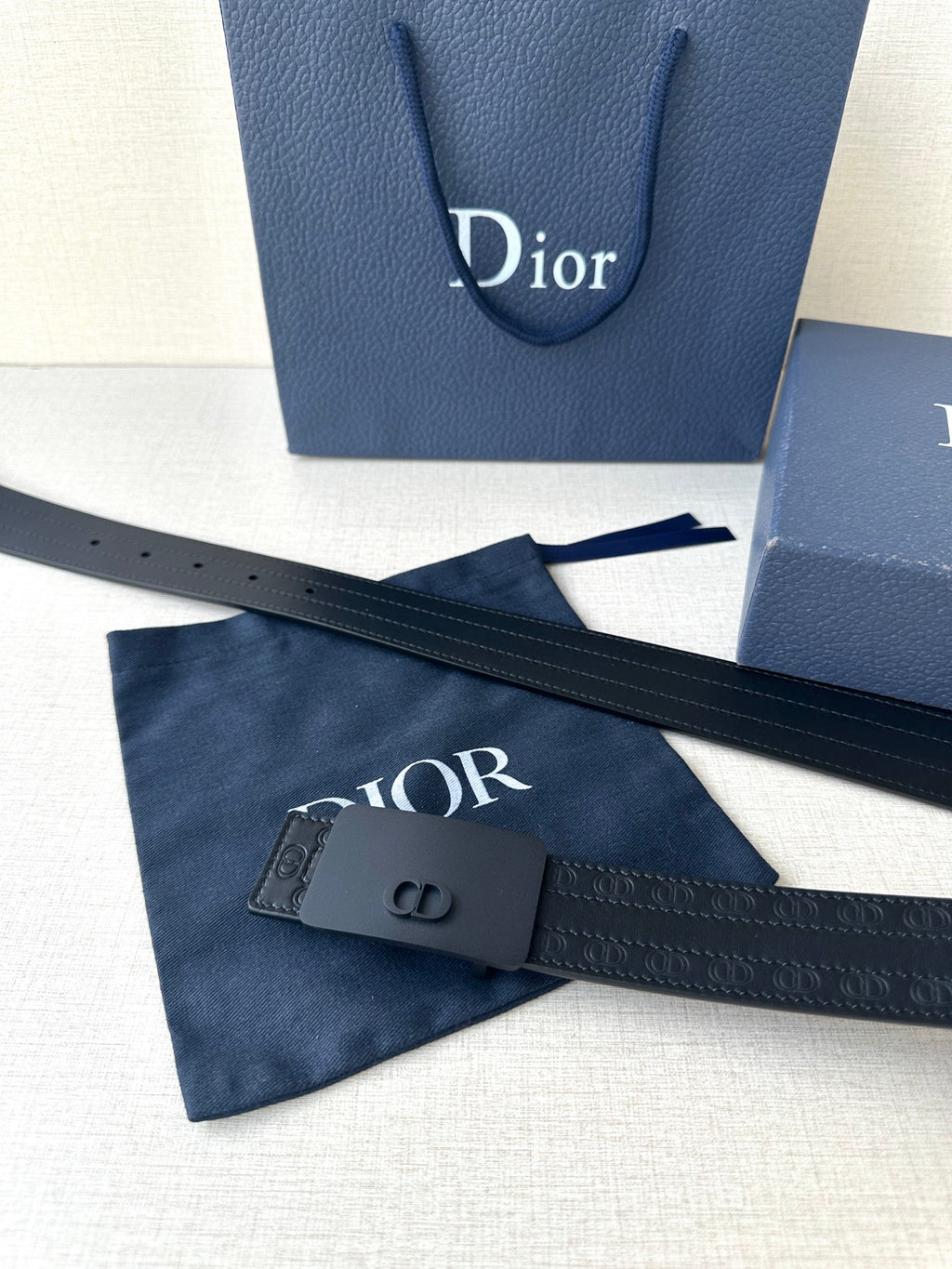 Leather belt with navy strap and dark CD buckle; shows textured embossed detail