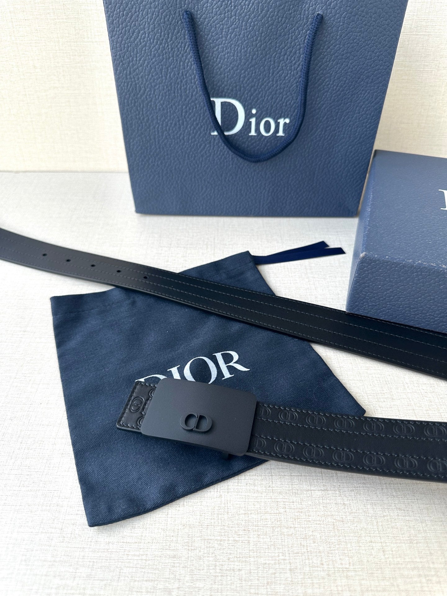 Leather belt with navy strap and dark CD buckle; shows textured embossed detail