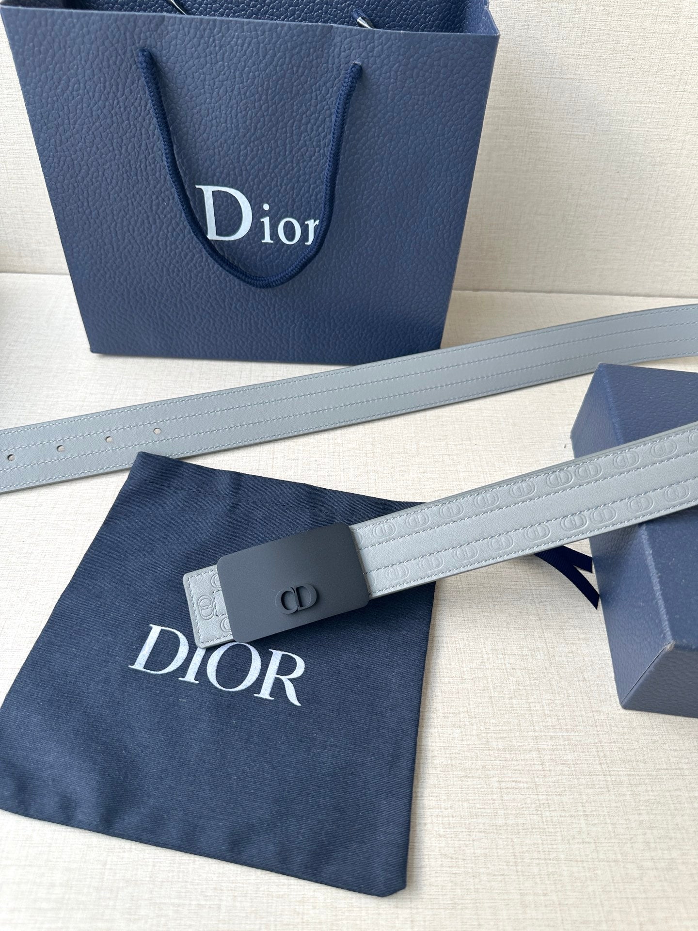 White leather belt with dark buckle and embossed logo strap, laid flat