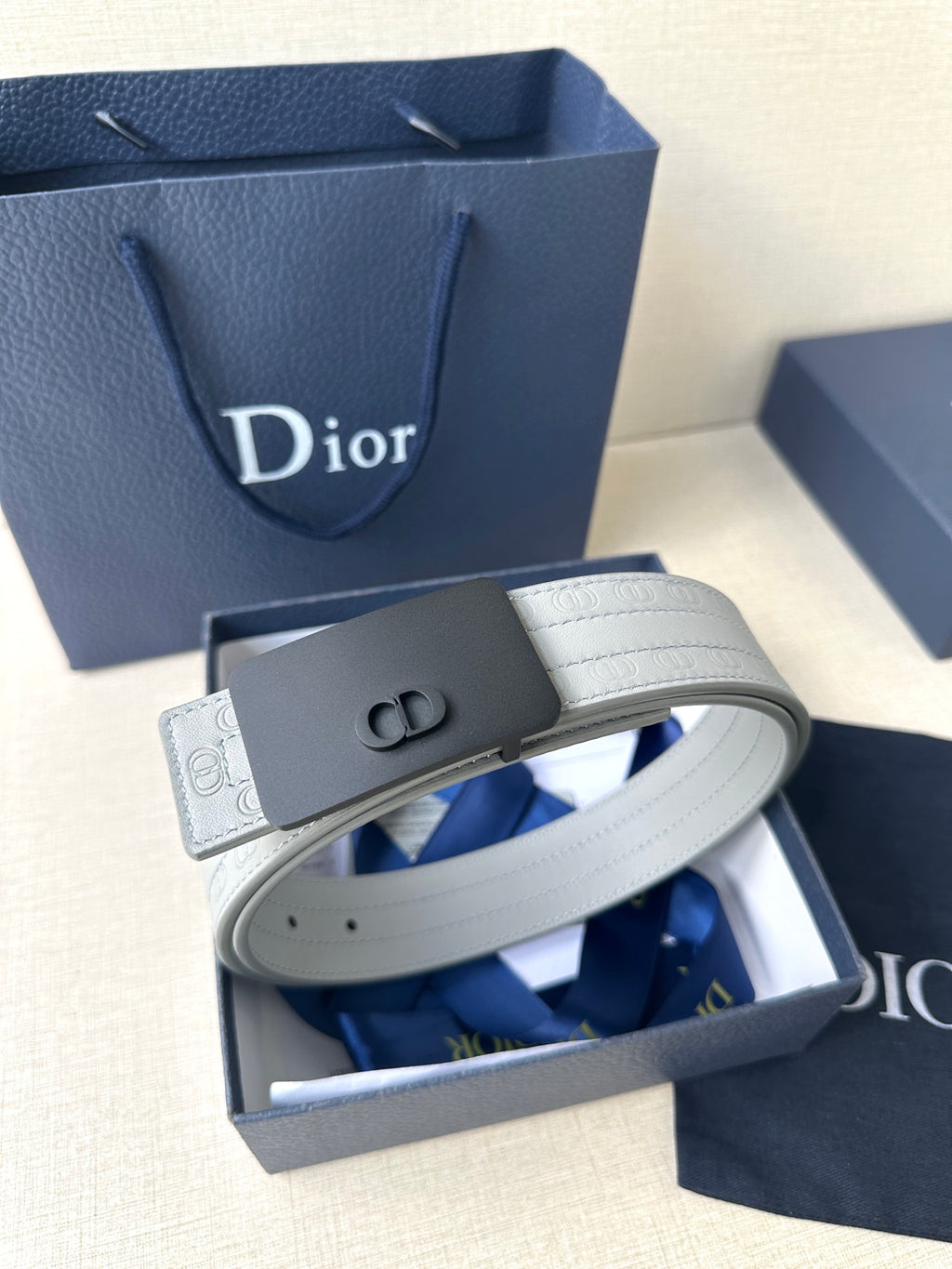 White leather belt with dark rectangular buckle and embossed Dior-style strap