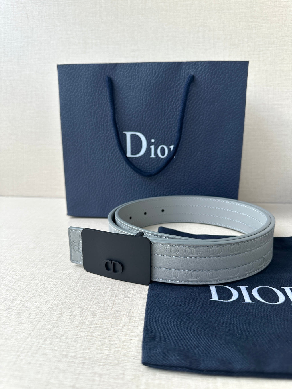 White leather belt with dark buckle and embossed strap pattern, angled close view