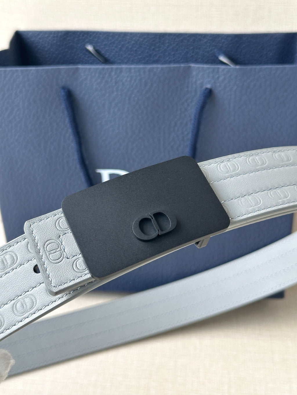 White leather belt with textured strap and dark rectangular buckle with oval emblem