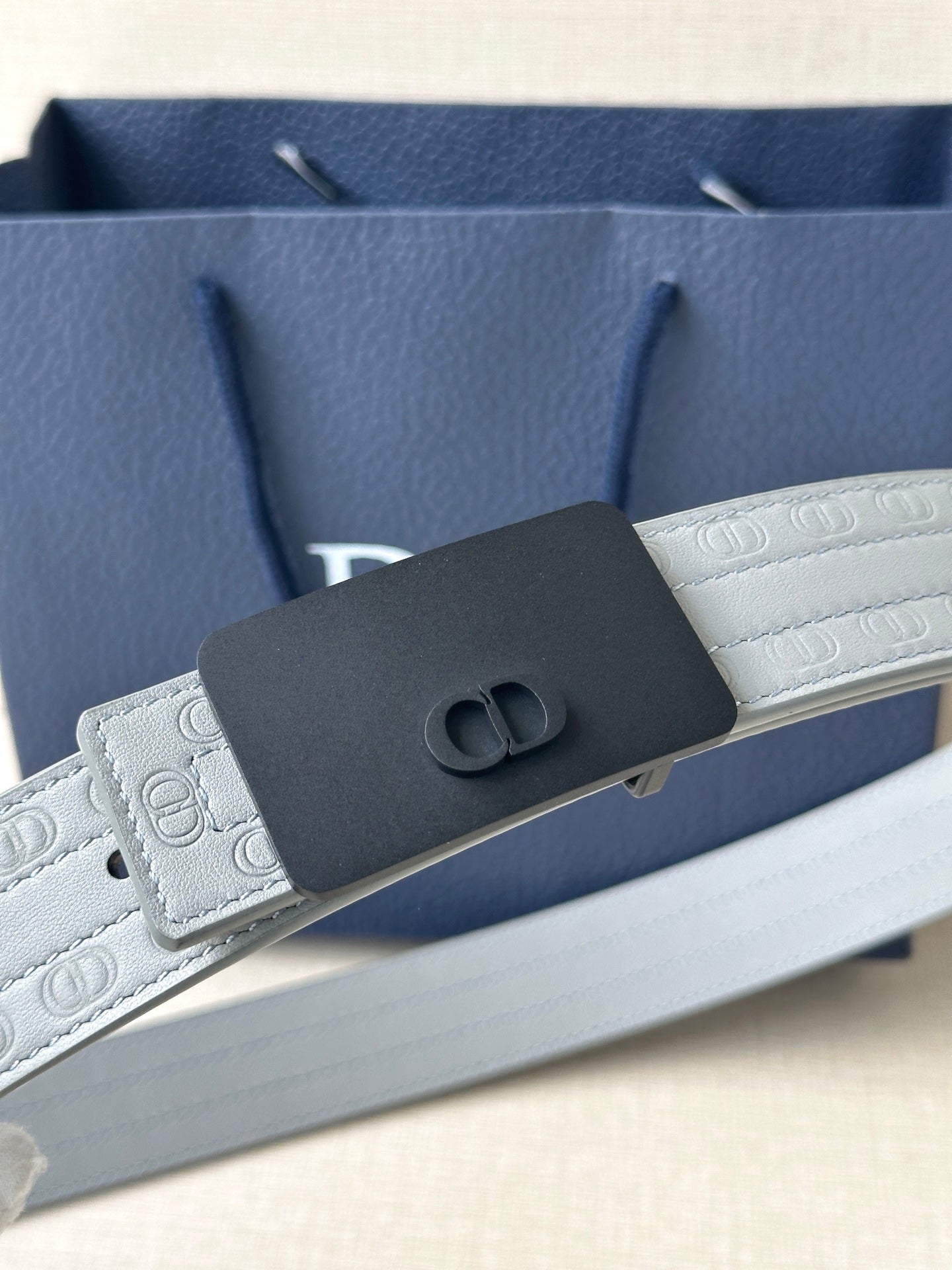 White leather belt with textured strap and dark rectangular buckle with oval emblem
