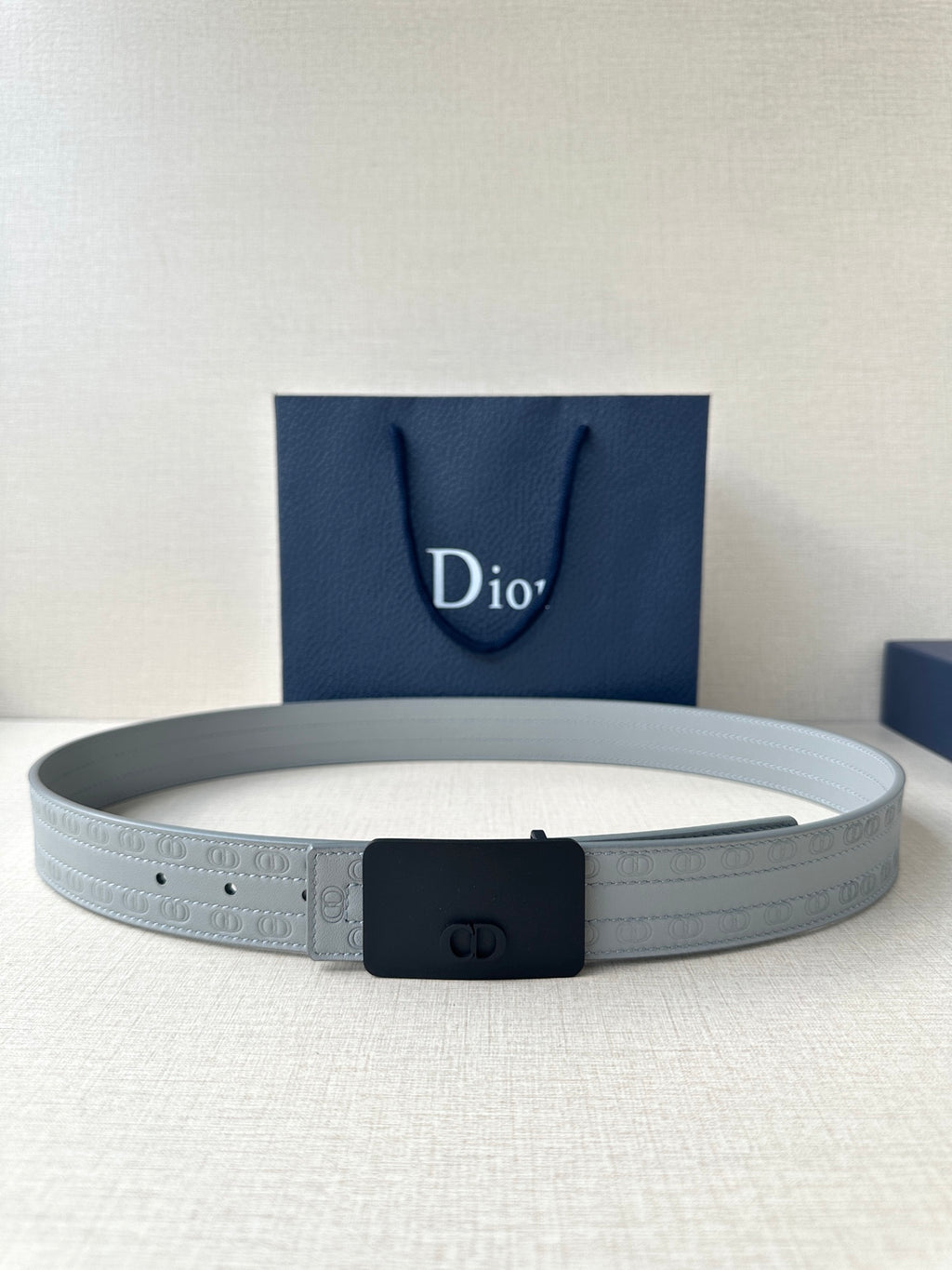 White leather belt with dark buckle and oval logo, adjustable holes