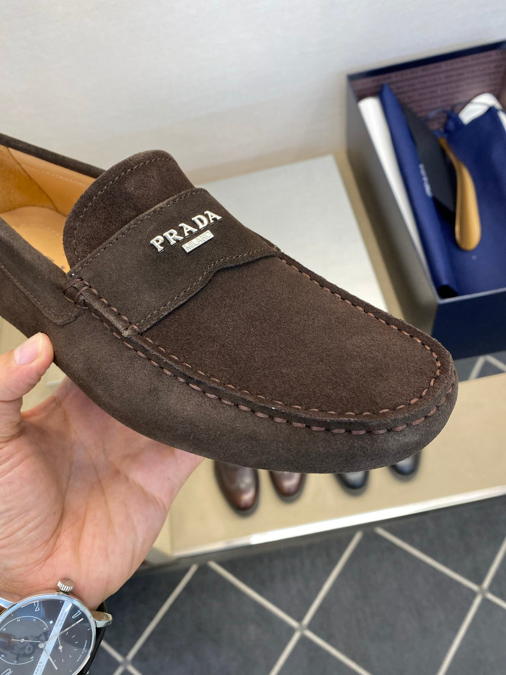 Close-up of brown suede loafer with Prada logo patch and contrast stitching
