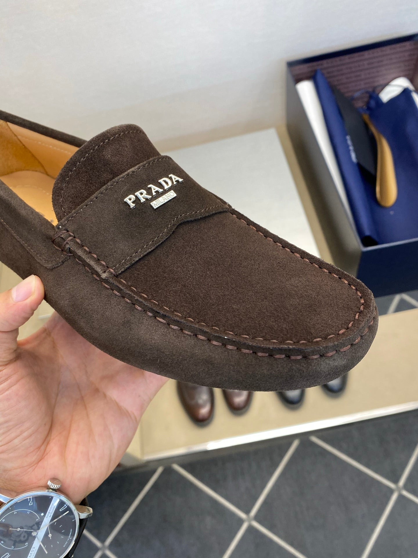 Close-up of brown suede loafer with Prada logo patch and contrast stitching