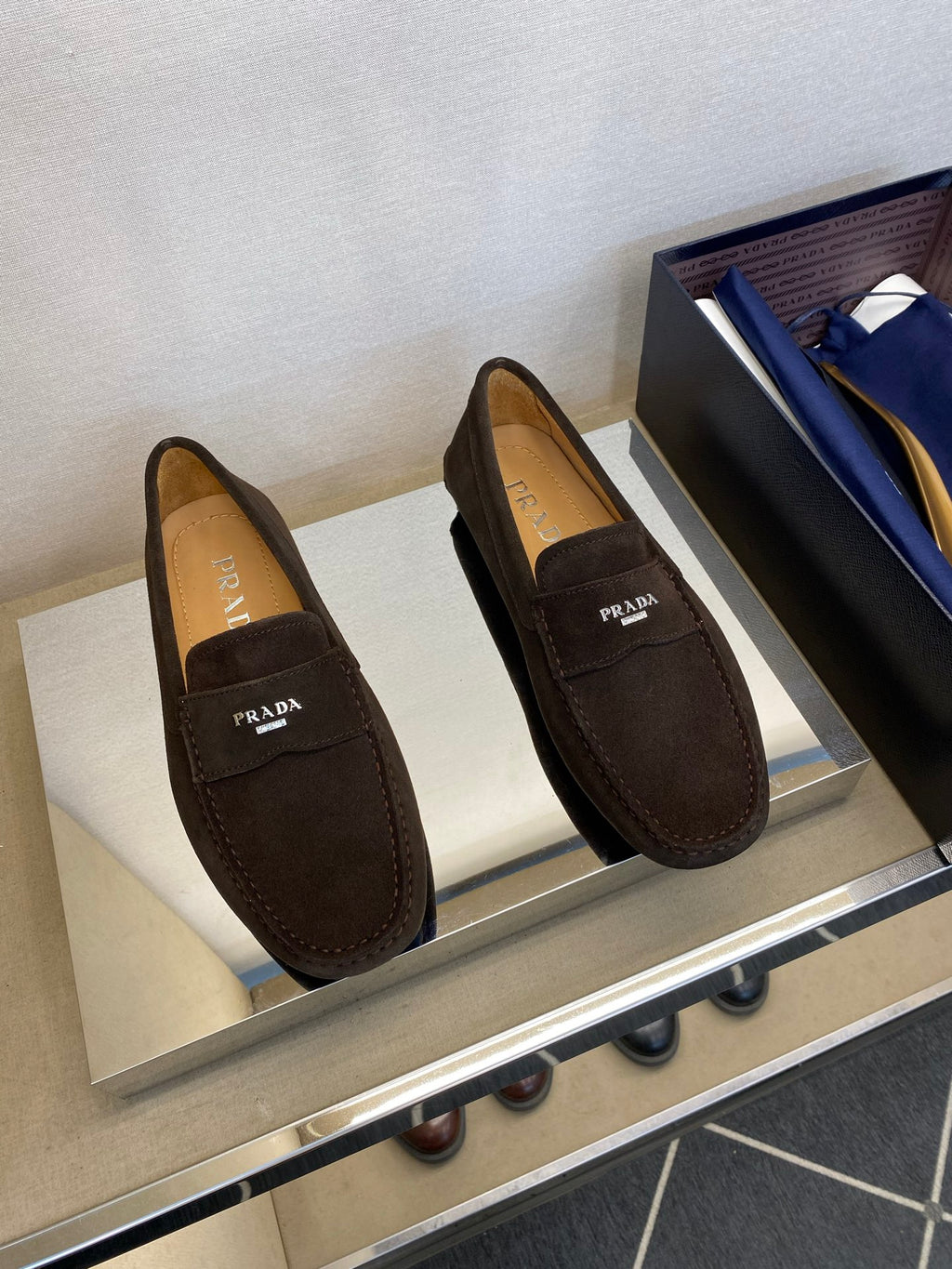 Brown suede loafers with Prada logo strap and stitched moccasin details